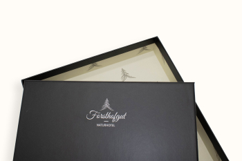 Schwarze Geschenkbox mit Logo des Naturhotels Forsthofgut und geöffnetem Deckel