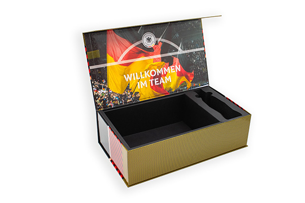 Geöffnete DFB-Box mit schwarzem Inlay und Deckelfoto mit Deutschlandfahnen im Stadion